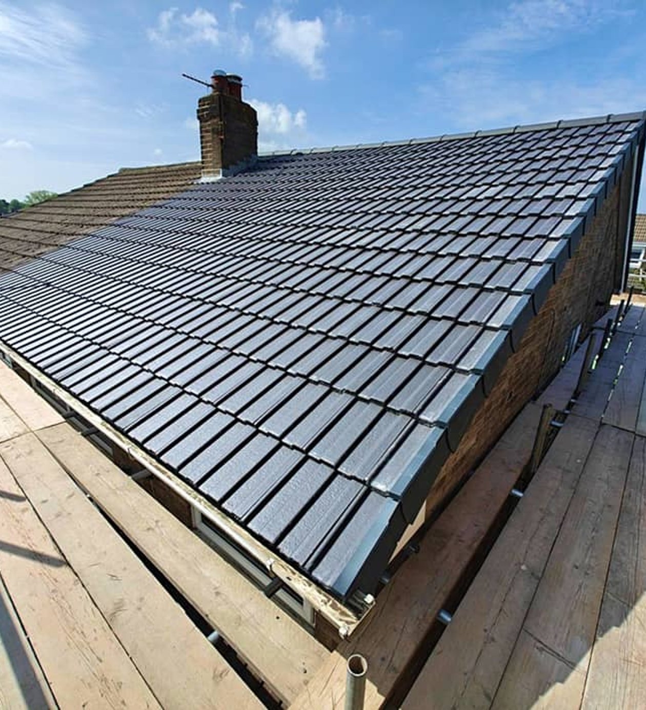 Gray tile roof installation on home with scaffolding