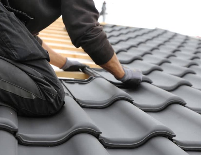 Roofer installing dark ceramic roof tiles