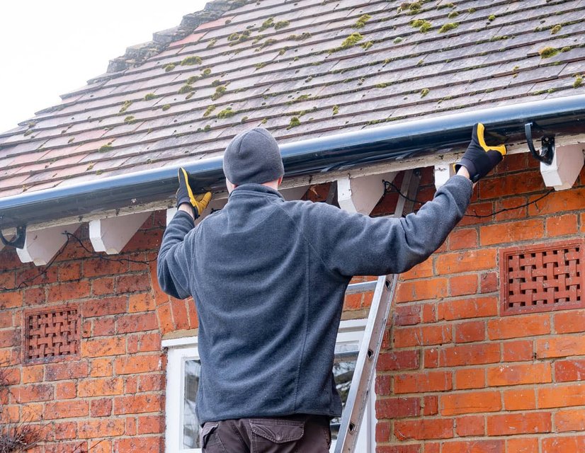 Worker on ladder installing gutters on brick house