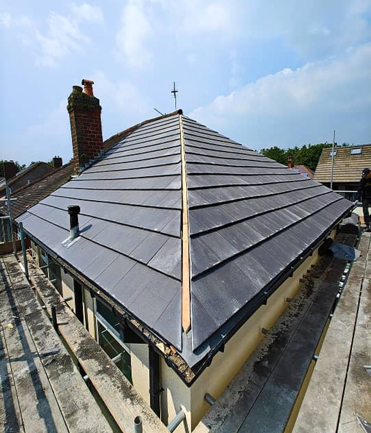 Completed dark slate hip roof beside scaffolding